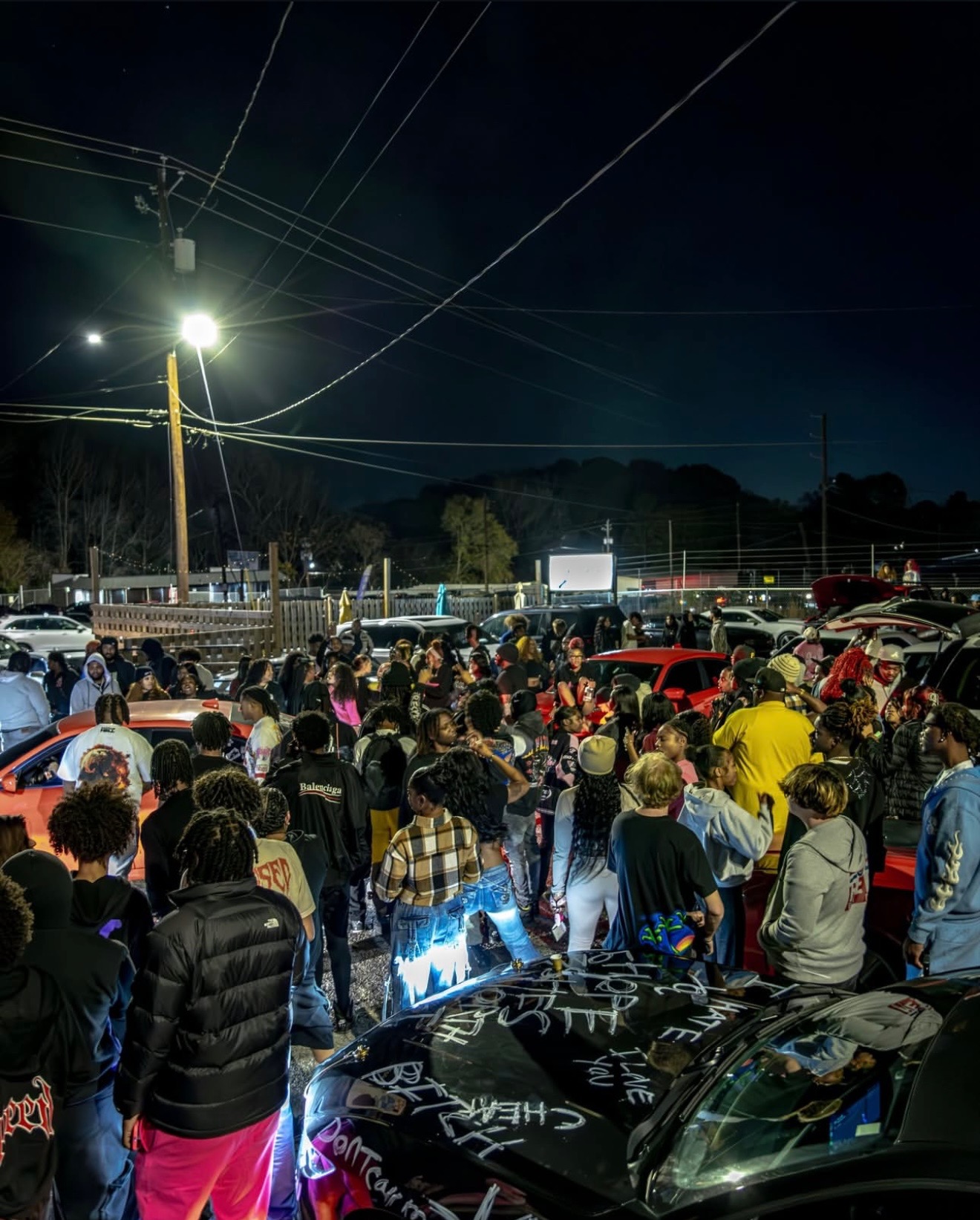 Night crowd gathered around cars at an N3wera pop-up event