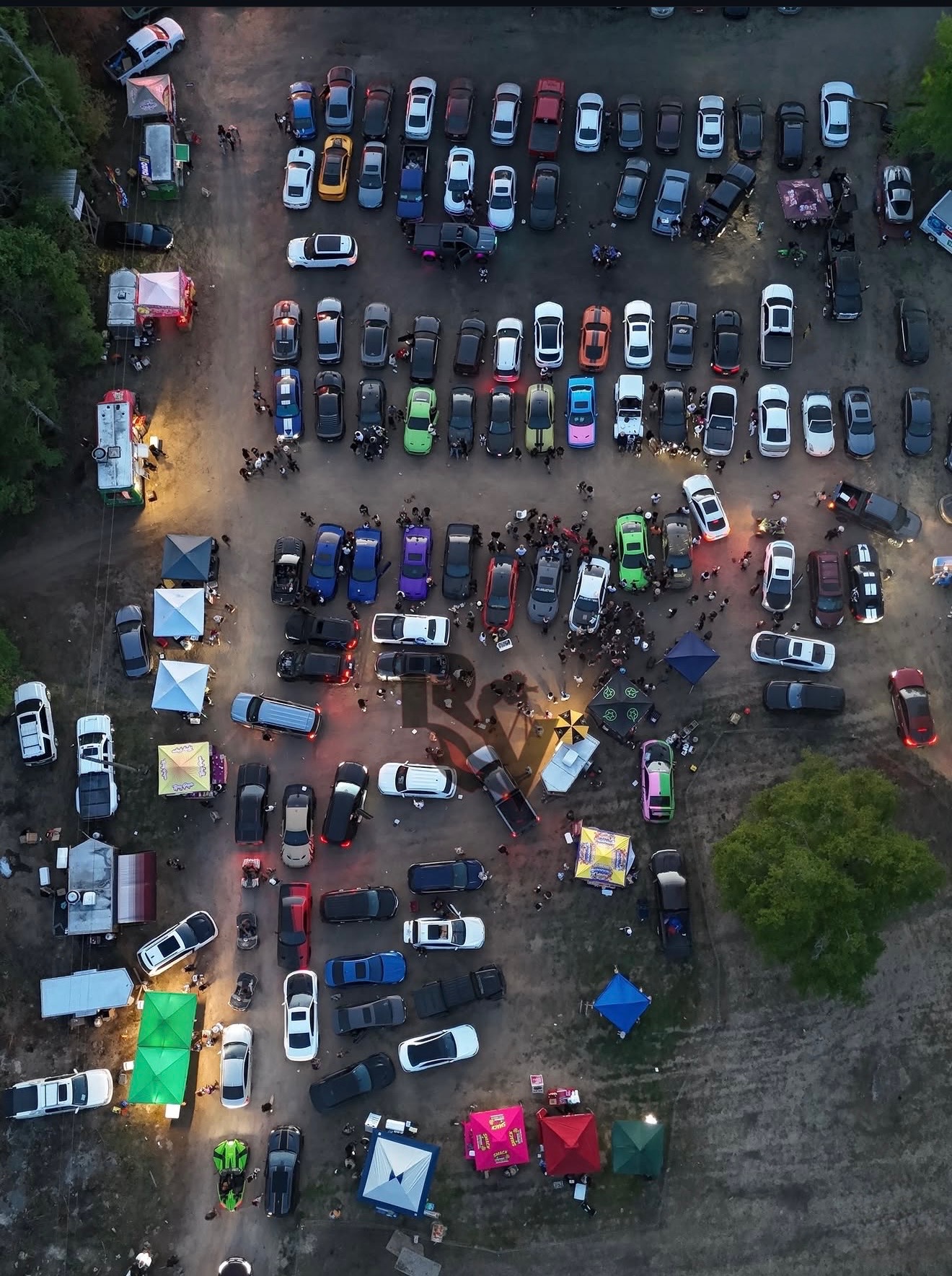 Aerial drone shot of a packed N3wera car meet with vendor tents at sunset